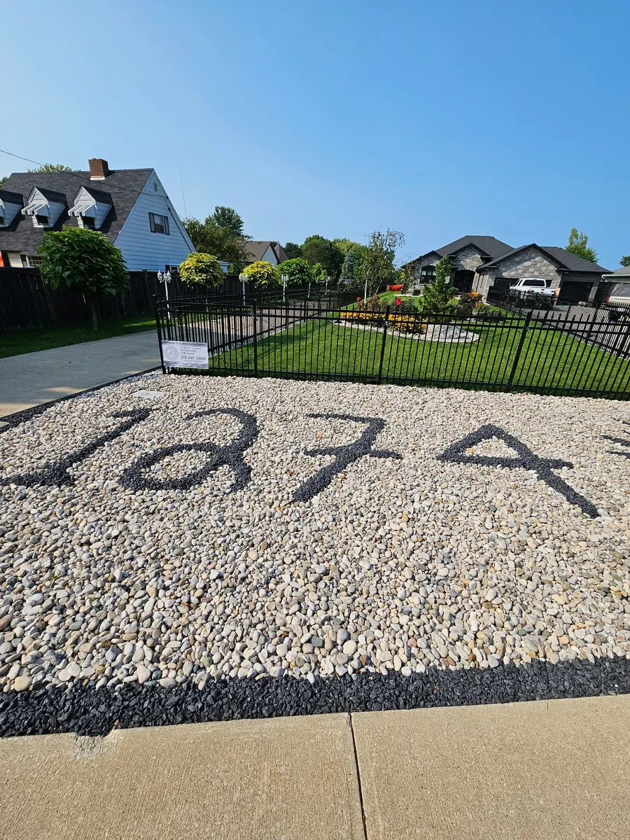 Black aluminum fence across a front yard with river stone