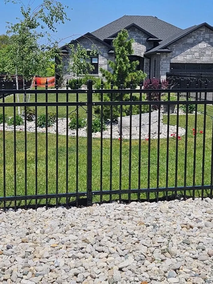 Black aluminum fence panels behind a stone landscape bed and cedar shrubs