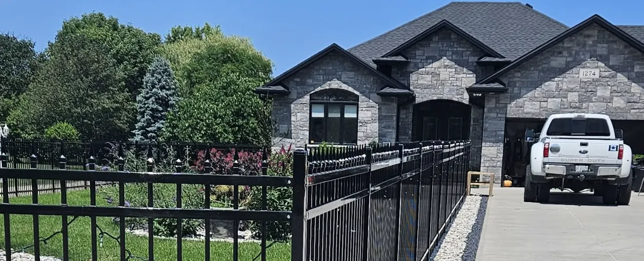 Stone home with a black aluminum fence and driveway in Sarnia